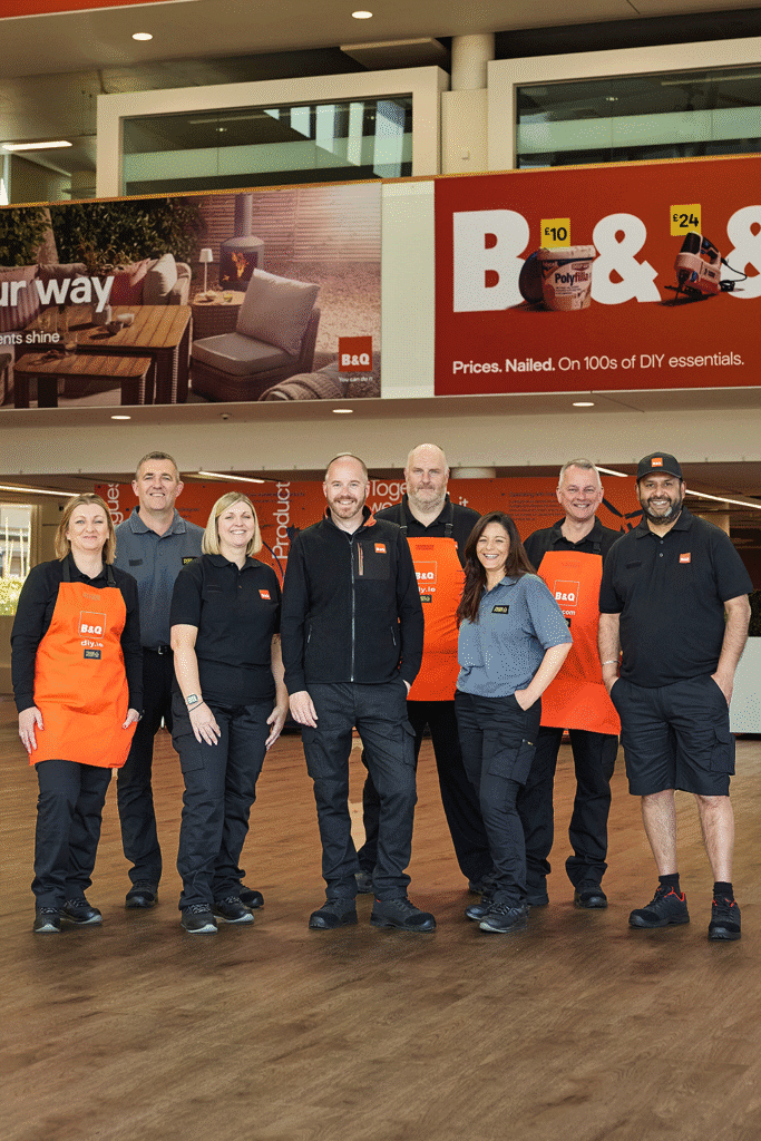 Group of B&Q staff wearing coordinated workwear inside a bright store environment, showcasing durable, sustainable-ready uniform styles designed for retail teams.